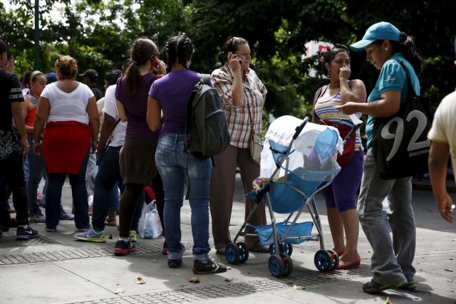 A woman with a baby stroller makes a phone call outside a drugstore to buy diapers in Caracas