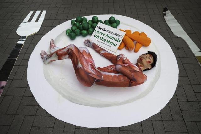 Un activista de la Sociedad Vegetariana de Hong Kong tumbado en un plato gigante junto a guisantes y zanahorias durante una manifestación en el distrito turístico de Tsim Sha Tsui, en Hong Kong (China), hoy, 23 de diciembre de 2015. Los activistas pidieron a los viandantes que extiendan su espíritu navideño a los animales y que reflexionen sobre la crueldad infligida a los animales criados para el consumo humano. EFE/Jerome Favre