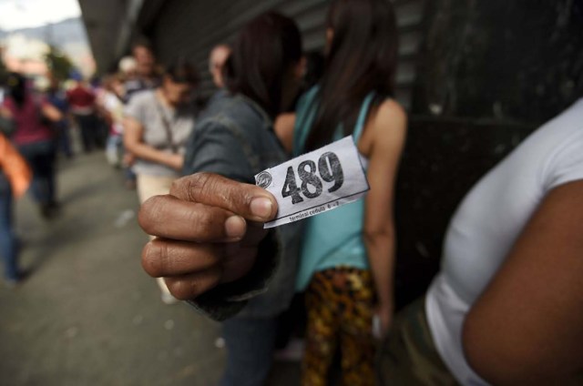 A woman holding a number to buy food waits outside a supermarket in Caracas, Venezuela on January 21, 2016. Trade unions demonstrated Wednesday outside the Venezuelan National Assembly against the economic emergency decrees issued by President Nicolas Maduro, who was meeting with the legislative commission studying whether parliament will approve the executive measures. AFP PHOTO/JUAN BARRETO / AFP / JUAN BARRETO