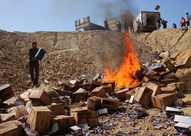 Un trabajador palestino rocía gasolina sobre cajas del chocolate Snickers en las afueras de la ciudad de Gaza, el jueves 10 de marzo de 2016. (Foto AP/Adel Hana)