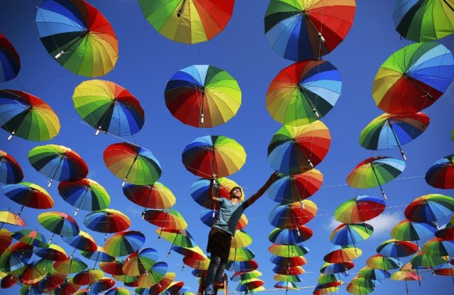 A Palestinian worker of a beachside coffeehouse decorates its terrace with hanging colourful umbrellas as part of decorations for the Muslim holy fasting month of Ramadan in Gaza City, on June 9, 2016. / AFP PHOTO / MOHAMMED ABED