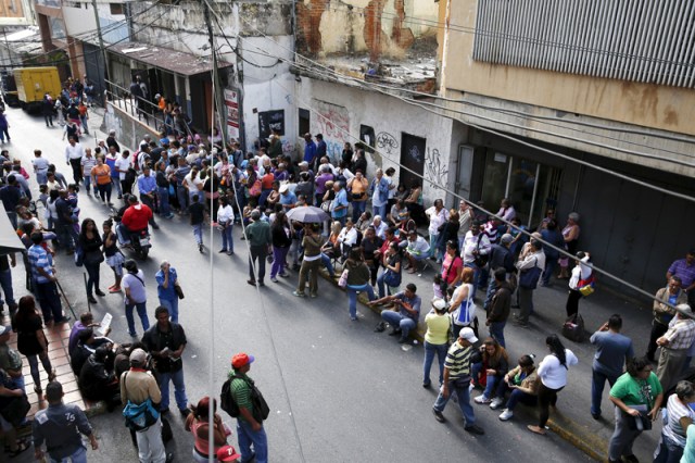 People queue to try to buy basic food items outside a supermarket in Caracas