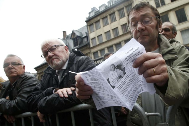 A mourner holds a leaflet with a picture of slain French parish priest Father Jacques Hamel durng a funeral ceremony at the Cathedral in Rouen, France, August 2, 2016.  Father Jacques Hamel was killed last week in an attack on a church at Saint-Etienne-du-Rouvray near Rouen that was carried out by assailants linked to Islamic State. REUTERS/Jacky Naegelen