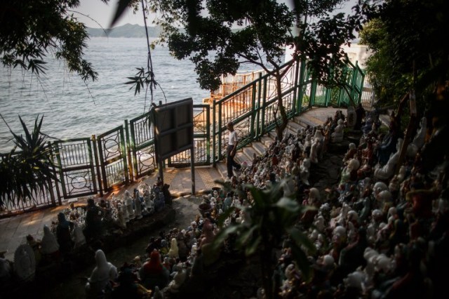 In this picture taken on August 9, 2016 dedicated volunteer Wong Wing-pong, an 85 year old retired butcher, walks past a display of unwanted statues of deities, gathered and repaired after their owners discarded them, on a rocky slope running down to the sea in Hong Kong. Religion and local customs permeate Hong Kong, where Buddhist and Taoist temples are common and incense offerings are regularly burned outside local businesses. Private homes often have a shrine to a local deity, with Christian churches and mosques also in the mix. But with space at a premium in a city were rents are sky high, informal collections of discarded gods often decorate roadsides and public spaces. / AFP PHOTO / Anthony WALLACE / To go with "HONG KONG-CULTURE-LIFESTYLE-RELIGION", FEATURE by Dennis Chong