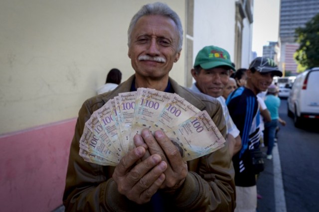 A man shows 100 Bolivar notes whilst queuing outside Venezuela's Central Bank (BCV) in Caracas in an attempt to change them, on December 16, 2016. Venezuelans lined up to deposit 100-unit banknotes before they turned worthless, but replacement bills had yet to arrive, increasing the cash chaos in the country with the world's highest inflation. Venezuelans are stuck in currency limbo after President Nicolas Maduro ordered the 100-bolivar note -- the largest denomination, currently worth about three US cents -- removed from circulation in 72 hours. / AFP PHOTO / FEDERICO PARRA