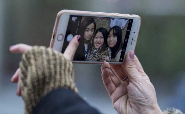 This picture taken on January 8, 2017 shows (from L-R) Peng Lin, Wang Peng and Hu Dongyuan posing for a selfie in the streets of Shanghai. Strolling a tree-lined Shanghai street with friends, Hu Dongyuan pulls out her smartphone and does what millions of Chinese women do daily: take a selfie, digitally "beautify" their faces, and pop it on social media. Such virtual makeovers, typically involving lightening skin, smoothing out complexions and rounding the eyes, have propelled selfie-editing app Meitu to the top ranks of China downloads. / AFP PHOTO / Johannes EISELE / TO GO WITH China-technology-lifestyle-apps-selfies-Meitu, FEATURE by Albee ZHANG