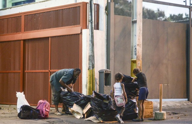 A man and two girls scavenge for food in the streets of Caracas on February 21, 2017. Venezuelan President Nicolas Maduro is resisting opposition efforts to hold a vote on removing him from office. The opposition blames him for an economic crisis that has caused food shortages. / AFP PHOTO / JUAN BARRETO / TO GO WITH AFP STORY BY Alexander Martinez