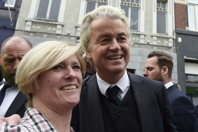 Dutch far-right Freedom Party leader (Partij Voor De Vrijheid, PVV) Geert Wilders is guarded by police as he poses with a supporter in Heerlen on March 11, 2017. Wilders was guarded by police as protesters took to the streets while he handed out pamphlets and posed for selfies as part of his election campaign. / AFP PHOTO / JOHN THYS