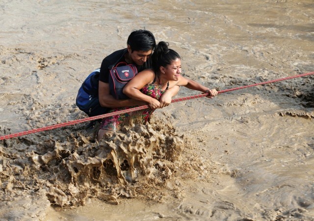 REFILE - CORRECTING NAME OF THE RIVER A woman is assisted while crossing a flooded street after the Huaycoloro river overflooded its banks sending torrents of mud and water rushing through the streets in Huachipa, Peru, March 17, 2017. REUTERS/Guadalupe Pardo