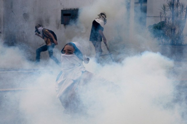 Venezuelan opposition activists protesting against President Nicolas Maduro's government are engulfed by a cloud of tear gas shot by riot police in Caracas on April 10, 2017.  Venezuela's political crisis intensified last week when the Supreme Court issued rulings curbing the powers of the opposition-controlled legislature. The court reversed the rulings days later, but the opposition intensified its protests from that moment.  / AFP PHOTO / FEDERICO PARRA