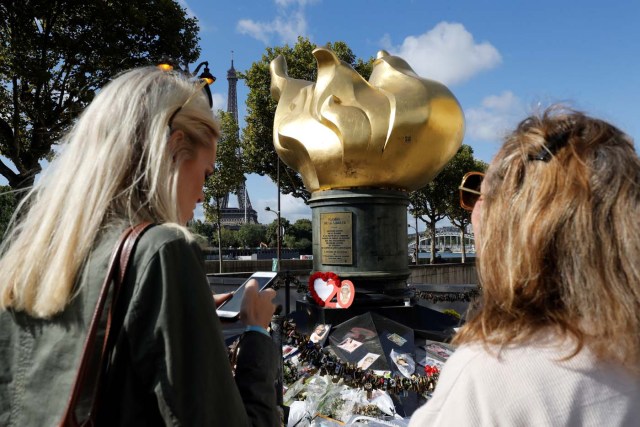 Women stand next to flowers, messages, pictures and locks laid around the Flame of Liberty monument - which became an unofficial memorial for Diana, Princess of Wales who died in a car crash in a nearby tunnel - over the Alma bridge in Paris on August 31, 2017, on the 20th anniversary of the death of the Princess. The life of Diana -- a shy, teenage aristocrat who suddenly became the world's most famous woman -- and her tragic death at 36 still captivates millions across the globe. Diana died in a car crash in Paris in the early hours of August 31, 1997, along with Dodi Fayed, her wealthy Egyptian film producer boyfriend of two months, and a drink-impaired, speeding driver Henri Paul, who was trying to evade paparazzi. / AFP PHOTO / Patrick KOVARIK