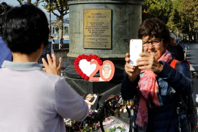 A woman takes a selfie next to the Flame of Liberty monument - which became an unofficial memorial for Diana, Princess of Wales who died in a car crash in a nearby tunnel - adorned with flowers, messages, pictures and locks, over the Alma bridge in Paris on August 31, 2017, on the 20th anniversary of the death of the Princess. The life of Diana -- a shy, teenage aristocrat who suddenly became the world's most famous woman -- and her tragic death at 36 still captivates millions across the globe. Diana died in a car crash in Paris in the early hours of August 31, 1997, along with Dodi Fayed, her wealthy Egyptian film producer boyfriend of two months, and a drink-impaired, speeding driver Henri Paul, who was trying to evade paparazzi. / AFP PHOTO / Patrick KOVARIK