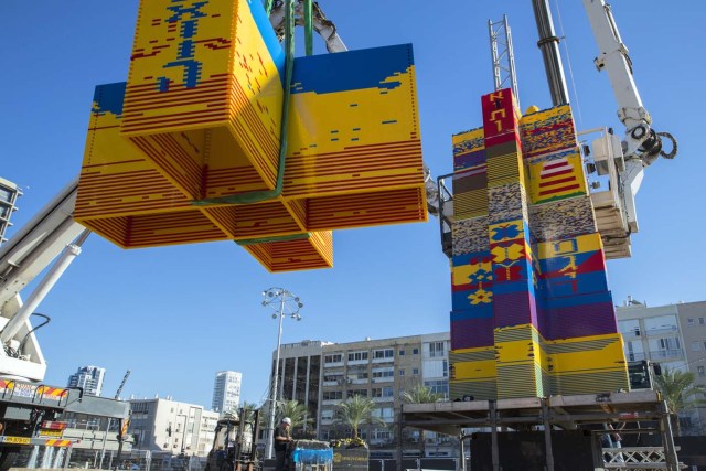 Workers and volunteers help assemble bricks during the construction of a LEGO tower in Tel Aviv's Rabin Square on December 26, 2017, as the city attempts to break Guinness world record of the highest such structure. / AFP PHOTO / JACK GUEZ