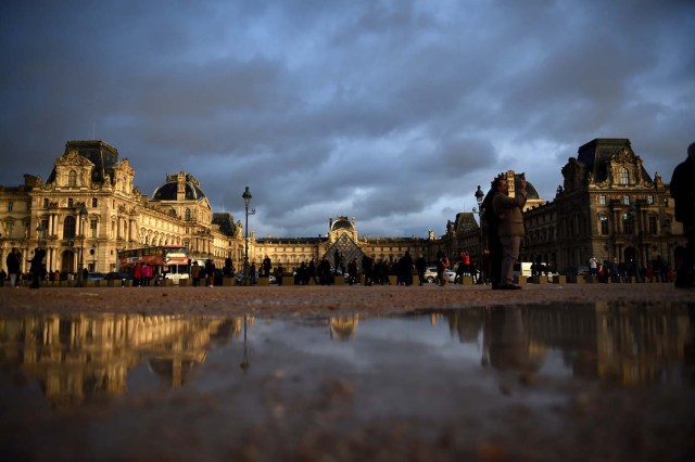 Tourists enjoy the scenery of the Louvre Museum and its pyramid under an overcast sky on January 1, 2018 in Paris. / AFP PHOTO / GUILLAUME SOUVANT