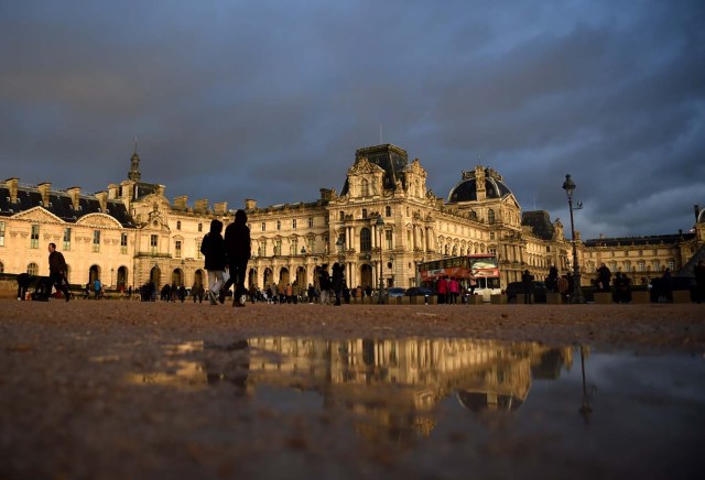 Tourists walk past the Richelieu wing of the Louvre Museum under an overcast sky on January 1, 2018 in Paris. / AFP PHOTO / GUILLAUME SOUVANT