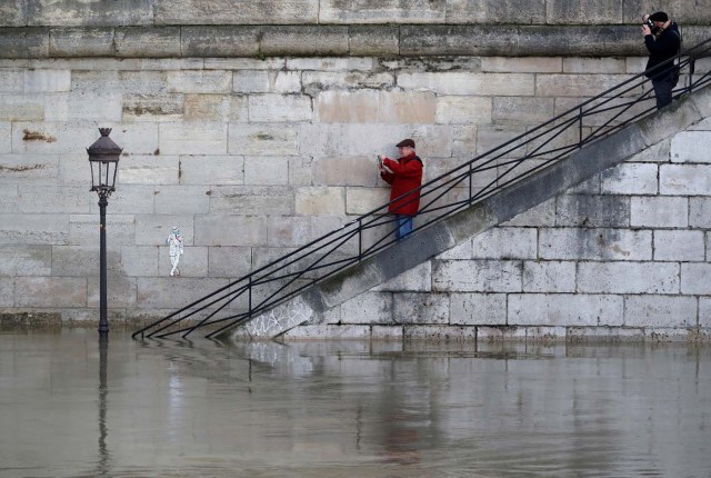 Men take pictures of a street lamp on the flooded banks of the River Seine in Paris, France, after days of almost non-stop rain caused flooding in the country, January 26, 2018. REUTERS/Christian Hartmann