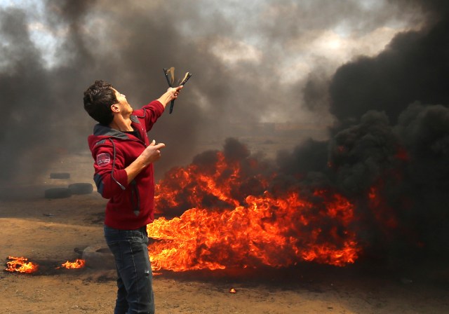Un palestino usa un tirachinas durante los enfrentamientos con las fuerzas israelíes a lo largo de la frontera con la franja de Gaza al este de Khan Yunis el 14 de mayo de 2018, mientras los palestinos protestan por la inauguración de la embajada de Estados Unidos tras su controvertido traslado a Jerusalén. / AFP PHOTO / SAID KHATIB