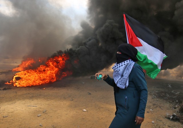 Un palestino sosteniendo su bandera nacional camina en el humo de las llantas incendiadas durante los enfrentamientos con las fuerzas israelíes a lo largo de la frontera con la franja de Gaza al este de Khan Yunis el 14 de mayo de 2018, mientras los palestinos protestan por la inauguración de la embajada muévete a Jerusalén / AFP PHOTO / SAID KHATIB