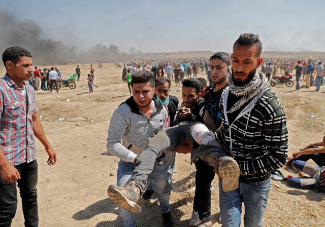 Los palestinos llevan a un manifestante herido durante enfrentamientos con fuerzas israelíes cerca de la frontera entre Gaza e Israel al este de la ciudad de Gaza el 14 de mayo de 2018, mientras los palestinos protestan por la inauguración de la embajada de Estados Unidos tras su controvertido traslado a Jerusalén. Al menos veintiocho palestinos fueron asesinados por disparos israelíes el 14 de mayo cuando decenas de miles protestaron y estallaron enfrentamientos a lo largo de la frontera de Gaza contra el traslado de su embajada a Jerusalén, dijo el Ministerio de Salud de Gaza. Fue el día más mortífero en el conflicto palestino-israelí desde la guerra de 2014 entre el Estado judío y los gobernantes islamistas de Gaza, Hamas. / AFP PHOTO / Thomas COEX