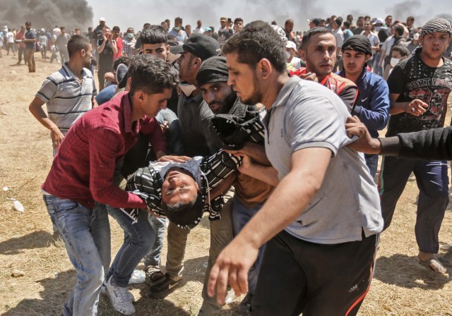 Los palestinos llevan a un hombre herido durante los enfrentamientos con las fuerzas israelíes cerca de la frontera entre Gaza e Israel al este de la ciudad de Gaza el 14 de mayo de 2018, mientras los palestinos protestan por la inauguración de la embajada de Estados Unidos tras su controvertido traslado a Jerusalén. Docenas de palestinos fueron asesinados por disparos israelíes el 14 de mayo cuando decenas de miles protestaron y estallaron enfrentamientos a lo largo de la frontera de Gaza contra la transferencia de su embajada a Jerusalén, luego de meses de protestas globales, ira palestina y elogios exuberantes de los israelíes por el presidente Donald Trump decisión dejando de lado décadas de precedentes. / AFP PHOTO / MAHMUD HAMS