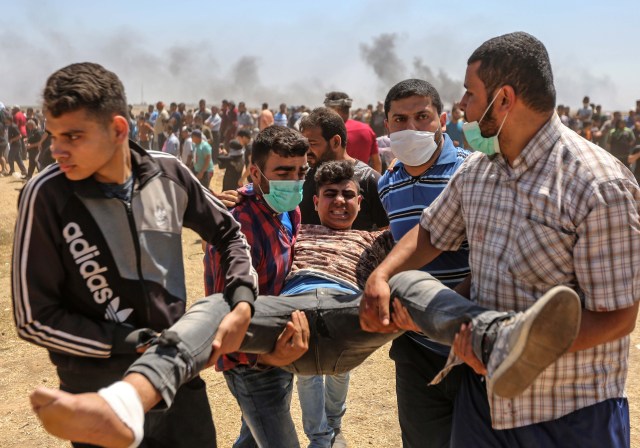 Los palestinos llevan a un manifestante herido durante los enfrentamientos con las fuerzas israelíes cerca de la frontera entre la franja de Gaza e Israel al este de la ciudad de Gaza el 14 de mayo de 2018, durante una manifestación el día de la mudanza de la embajada de EE. UU. A Jerusalén. Docenas de palestinos fueron asesinados por disparos israelíes el 14 de mayo cuando decenas de miles protestaron y estallaron enfrentamientos a lo largo de la frontera de Gaza contra la transferencia de su embajada a Jerusalén, luego de meses de protestas globales, ira palestina y elogios exuberantes de los israelíes por el presidente Donald Trump decisión dejando de lado décadas de precedentes. / AFP PHOTO / MAHMUD HAMS