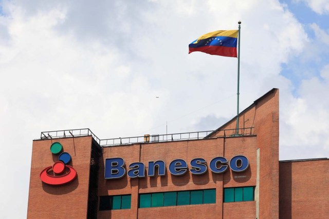 A Venezuelan flag waves above the corporate logo of Banesco bank at one of their office complexes in Caracas, Venezuela May 2, 2018. Picture taken May 2, 2018. REUTERS/Marco Bello